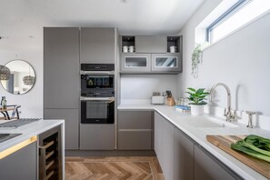 A modern kitchen with built-in appliances, a white countertop, and a window providing natural light. - 2 Bed in Bude (oc-b588787) (Bude)