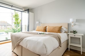 Ein modernes Schlafzimmer mit einem großen Bett, zwei Nachttischlampen, einem Nachttisch und Blick ins Freie.