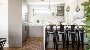 Una cucina moderna con isola centrale, sgabelli da bar, lampade a sospensione e pavimento in legno a spina di pesce.