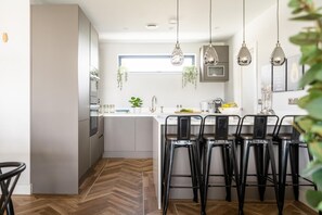 Eine moderne Küche mit einer zentralen Kochinsel, Barhocker, hängenden Pendelleuchten und einem Fischgrätenparkettboden.