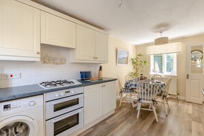 Une cuisine avec des meubles blancs, une cuisinière à gaz, un lave-linge et un coin repas comprenant une table et des chaises.