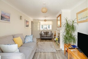 A living room with a grey sofa, a grey armchair, a wooden coffee table, a TV, and a large green plant. - 3 Bed in Bridport (oc-b45261) (Bridport)