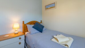 A bedroom with a single bed, a nightstand with a lamp, a framed picture on the wall, and a window. - 3 Bed in Bridport (oc-b45261) (Bridport)