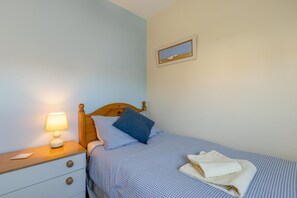 Ein Schlafzimmer mit einem Einzelbett, einem Nachttisch mit Lampe, einem gerahmten Bild an der Wand und einem Fenster.