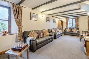 A cozy living room with a fireplace, leather sofas, a chess table, and a view through a window. - 5 Bed in Grizebeck (oc-b34029) (Kirkby Ireleth)