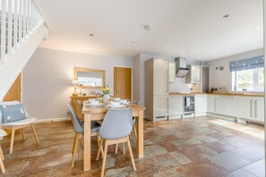 Eine moderne Küche mit weißen Schränken, ein Essbereich mit einem Holztisch und Stühlen sowie eine Treppe, die zu einer oberen Ebene führt.