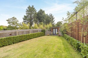 Ein Garten mit Holzzaun, kleiner Gartenhütte und gepflegtem Rasen.