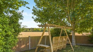 A wooden swing set in a backyard with a wooden fence and trees. - 3 Bed in Briningham (oc-s44878) (Briningham)