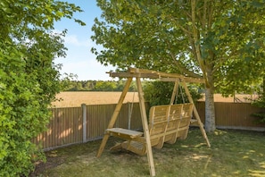 Eine Holzschaukel im Garten, mit Holzzaun und Bäumen.