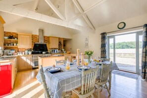 A modern kitchen with a dining area, wooden cabinets, and a large window offering a view of the outdoors. - 3 Bed in Briningham (oc-s44878) (Briningham)