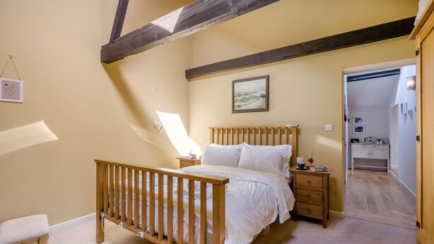 A bedroom with a wooden bed, a nightstand, a bedside table, a crib, and a painting on the wall. - 3 Bed in Briningham (oc-s44878) (Briningham)