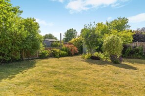 Ein Garten mit Holzzaun, Gartenhaus und verschiedenen Sträuchern und Bäumen.