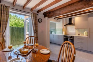 A dining area with a table set for breakfast, a kitchen with modern appliances, and a view of the outdoors. - 2 Bed in Melton Mowbray (oc-h45352) (Hose)