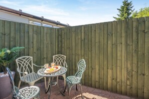 A patio area with a wooden fence, a round table with chairs, and a potted plant. - 2 Bed in Melton Mowbray (oc-h45352) (Hose)