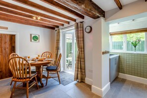 A dining area with a wooden table and chairs, a kitchen with a window, and a door leading outside. - 2 Bed in Melton Mowbray (oc-h45352) (Hose)