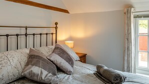 Ein Bett mit Kopfteil, Kissen, einer Nachttischlampe und einem Fenster mit Vorhängen.