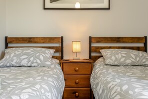 A double bed with leaf-patterned bedding, a bedside table with a lamp, and a framed picture on the wall. - 2 Bed in Melton Mowbray (oc-h45352) (Hose)
