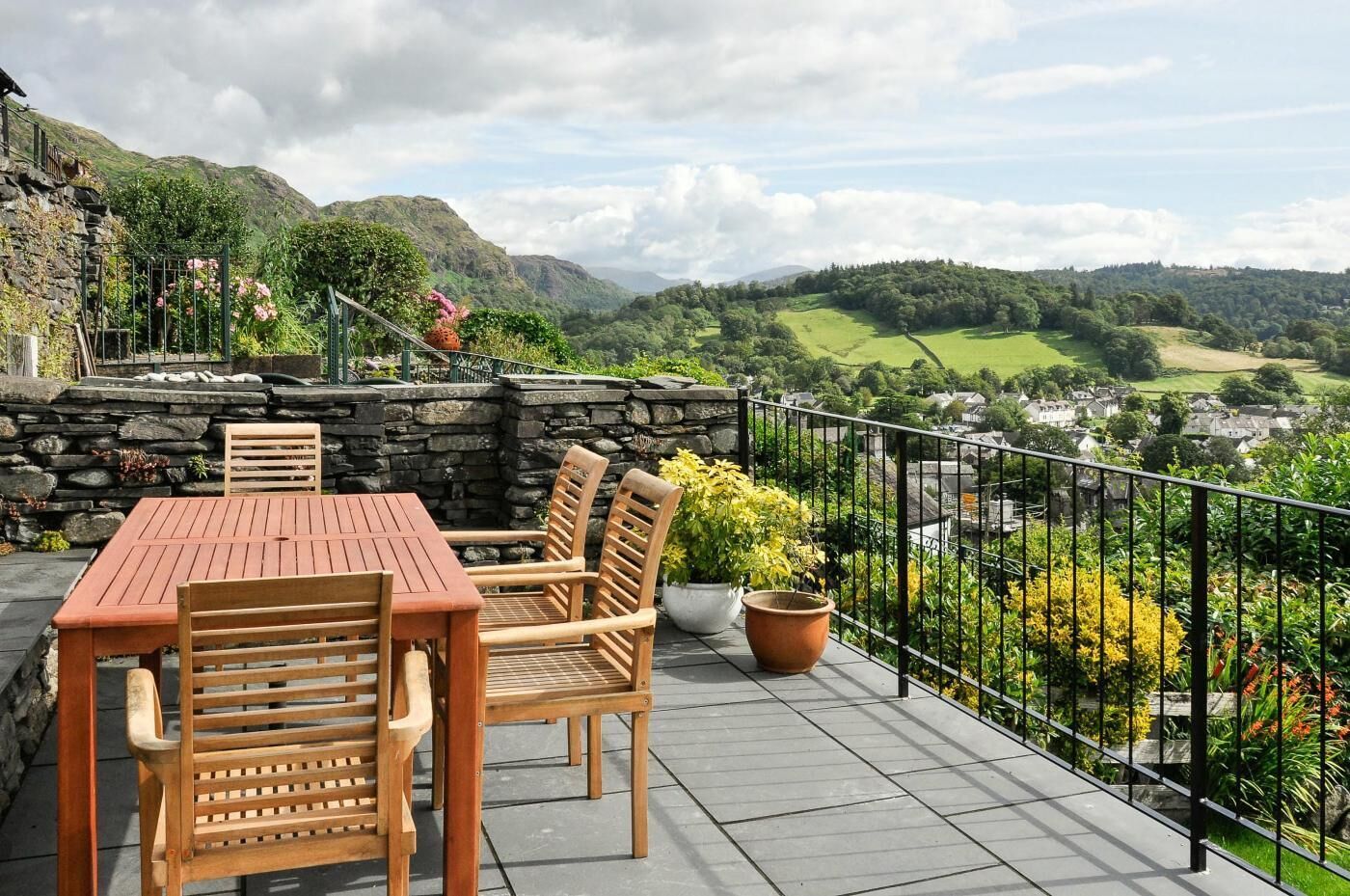 Eine Terrasse mit einer Steinmauer, einem Holztisch und -stühlen sowie Blick auf ein Tal und eine Stadt.