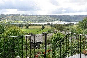 A view from a balcony with a metal railing, overlooking a green landscape with fields, trees, and a lake. - 3 Bed in Coniston (oc-lr149) (Coniston)