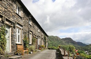 A stone cottage with a paved driveway, a wooden bench, and potted plants. - 3 Bed in Coniston (oc-lr149) (Coniston)