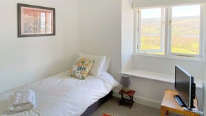 Et soveværelse med seng, et vindue, et fjernsyn på et stativ og et billede i ramme på væggen.