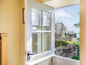 A room with a large window offering a view of a stone wall and greenery outside. - 2 Bed in Scarborough (oc-36571) (Ebberston)