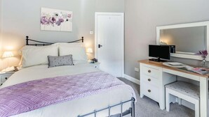 Ein Schlafzimmer mit einem Bett, Nachttischlampen, einem Schreibtisch mit Computer und einer Tür.