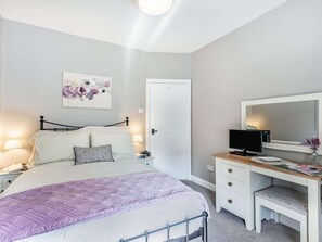 Ett sovrum med en säng, sänglampor, ett skrivbord med en dator och en dörr.