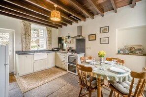 Uma cozinha com armários brancos, uma mesa de jantar para quatro pessoas e um lustre.