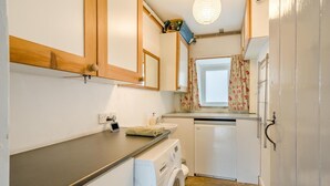 A compact kitchen with a washing machine, a small sink, and a window with floral curtains. - 2 Bed in Sedbusk (oc-l44913) (Sedbusk)