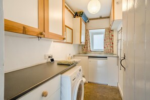 Uma cozinha compacta com máquina de lavar, uma pia pequena e uma janela com cortinas florais.
