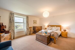 Quarto com cama, mesas de cabeceira, cômoda de madeira, uma cadeira e janela com cortinas.