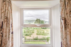Ein Fenster mit Blick auf eine ländliche Landschaft, darunter ein Hügel und ein Baum.