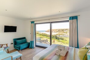 Ein Hotelzimmer mit einer großen Schiebeglaswand, einer Couch, einem Bett mit aufgerollten Handtüchern und einem Flachbildfernseher.