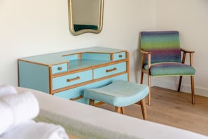Ein Zimmer mit einer hellblauen Kommode mit Schubladen, einer passenden Bank, einem bunten Stuhl und einem Spiegel an der Wand.