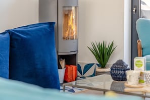 Ein modernes Wohnzimmer mit Kamin, einem blauen Sofa, einer Pflanze und einem Couchtisch mit Büchern und einer Tasse.