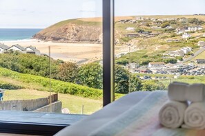 Blick aus einem Fenster auf einen Strand und ein Wohngebiet mit Häusern und geparkten Autos.