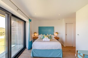 Ein modernes Schlafzimmer mit einem großen Bett, zwei Nachttischlampen, Blick durch eine Schiebetür und einer Wand in Türkis.
