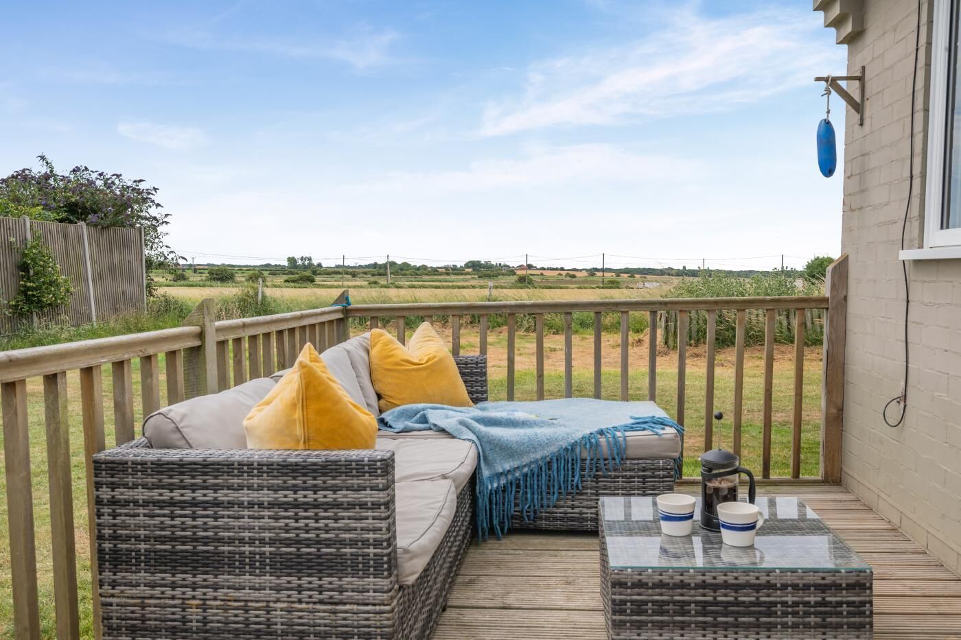 A wicker sofa with cushions, a glass table with a cup, and a view of a field.