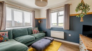 Ein modernes Wohnzimmer mit einem Ecksofa, einer Bank, einem Fernseher und einer hängenden Pflanze.