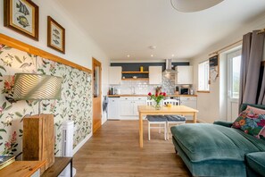 A modern kitchen with white cabinets, a wooden dining table, and a green sofa. - 1 Bed in Eccles-on-Sea (oc-w45218) (Lessingham)