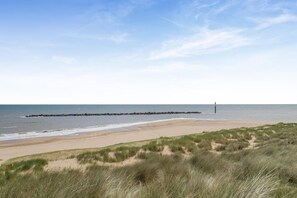 A beach with a dune system and a rocky breakwater extending into the sea.
