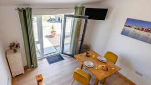 Uma sala de jantar com uma mesa posta para dois, uma televisão na parede e vista para o exterior através das portas de vidro.