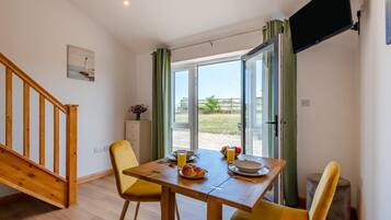 A dining area with a wooden table, yellow chairs, and a view of the outdoors through a glass door.