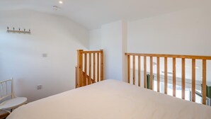 Quarto com uma cama grande, uma cadeira de madeira, uma mesa pequena e um lance de escadas com corrimão de madeira.
