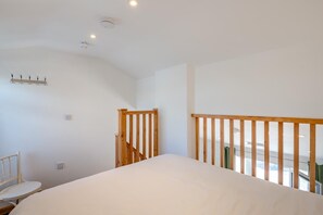 Ein Schlafzimmer mit einem großen Bett, einem Holzstuhl, einem kleinen Tisch und einer Treppe mit hölzernem Geländer.