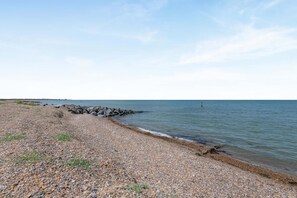 Ein Kiesstrand mit einem steinernen Wellenbrecher, der sich ins Wasser erstreckt.