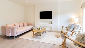 Una sala de estar moderna con un sofá, una mesa de centro, una silla, un televisor de pantalla plana montado en la pared y una lámpara.