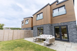A modern two-story house with a patio area featuring outdoor furniture. - 3 Bed in Watergate Bay (oc-b642096) (Tregurrian)