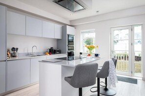 Eine moderne Küche mit einer zentralen Kochinsel, einem eingebauten Backofen und einem Fenster mit Blick auf einen Garten.